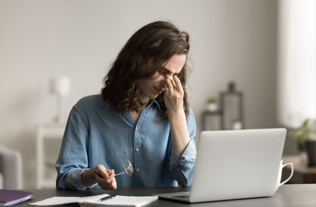 A woman working at a computer rubs her dry eyes as she experiences irritation from meibomian gland dysfunction.