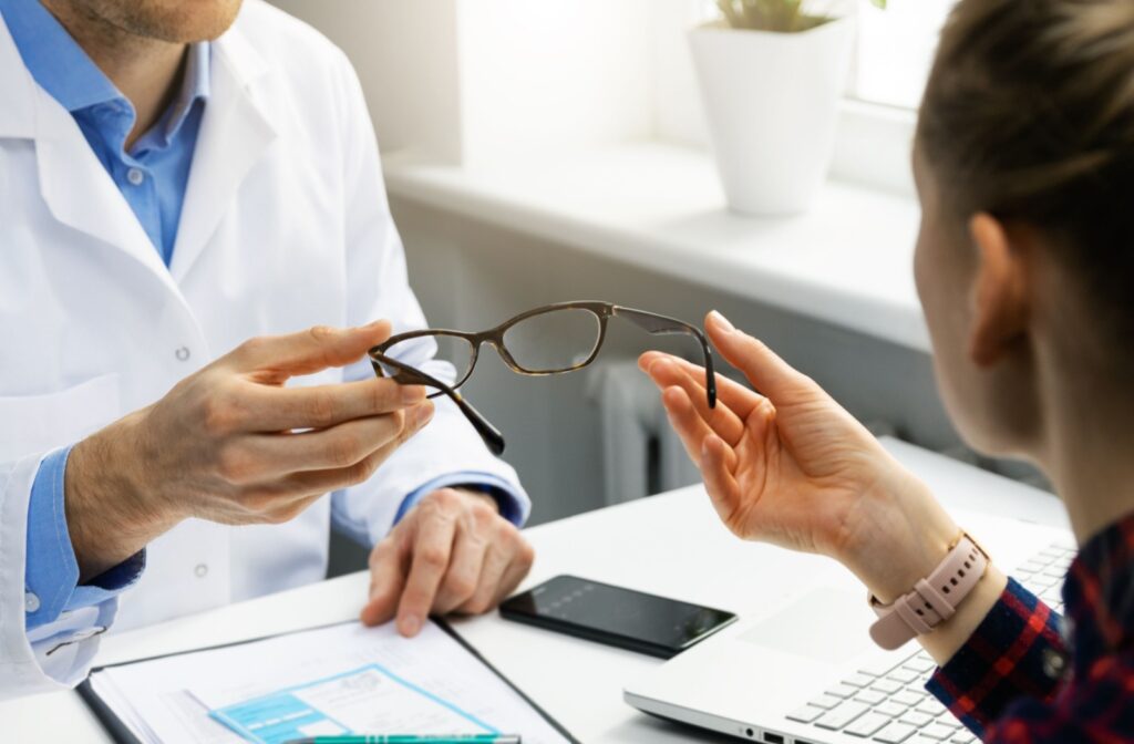 An optometrist sitting across their desk from a patient and handing them their new pair of glasses.
