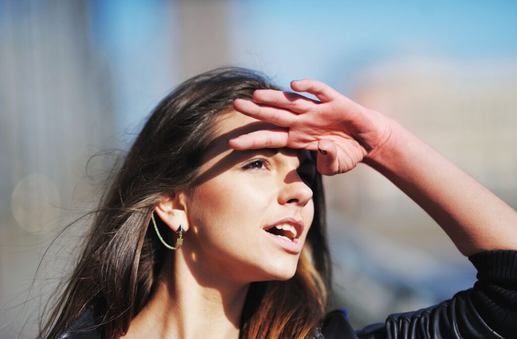A young adult raising a hand to shield their eyes while outdoors due to light sensitivity.