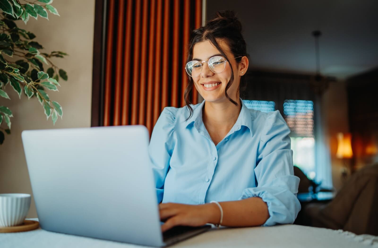A business professional smiles while working on their laptop from home due to their Neurolens glasses relieving neck pain
