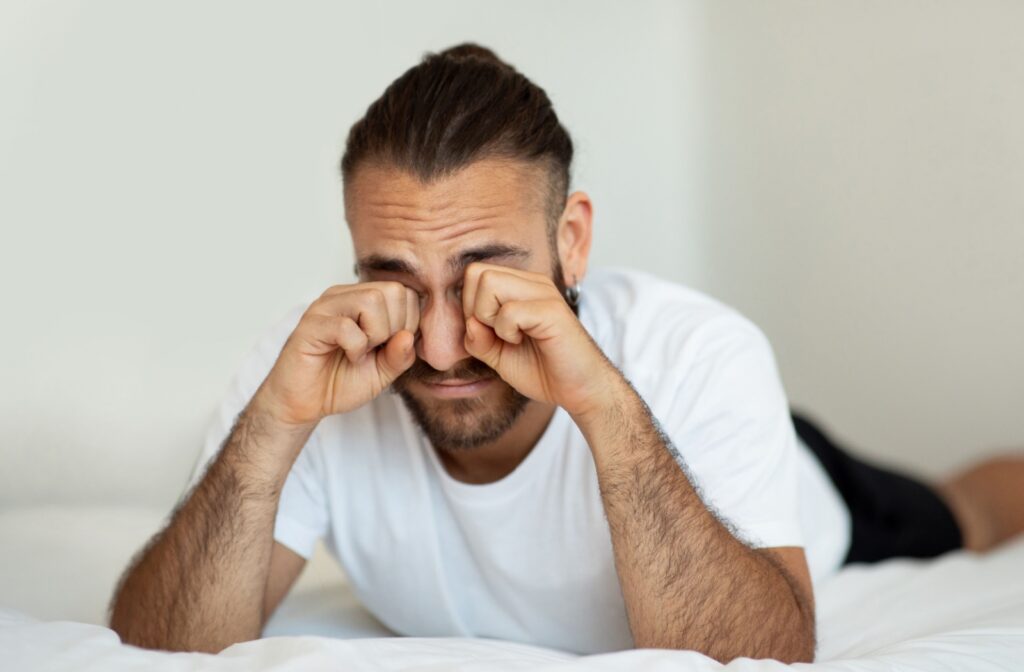 Adult rubbing their eyes in bed after waking up with blurry vision